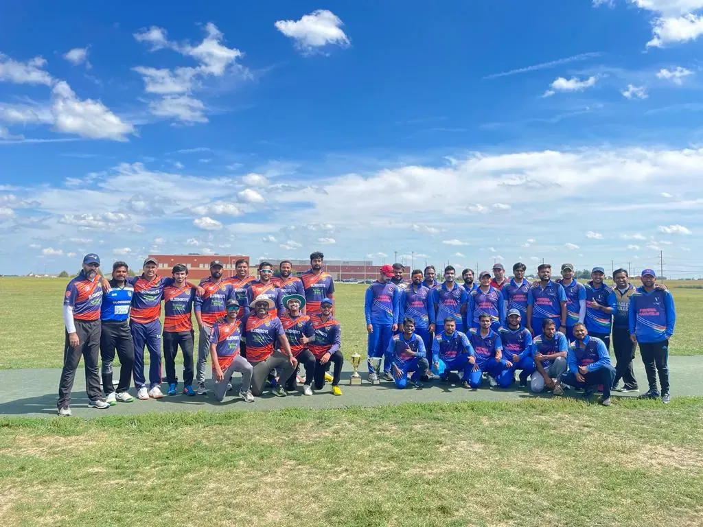 Cricket teams standing together on an outdoor field beneath a blue sky.